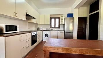 Una cocina con armarios blancos, microondas, lavadora, lavavajillas y refrigerador.