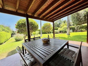 An outdoor patio with a wooden table and chairs, surrounded by a lush garden and a clear view of the sky. - 152 PER - Stay Perla House (Paralimni)