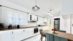 Een moderne keuken met witte kasten, een houten aanrecht en een eethoek met een tafel en stoelen.
