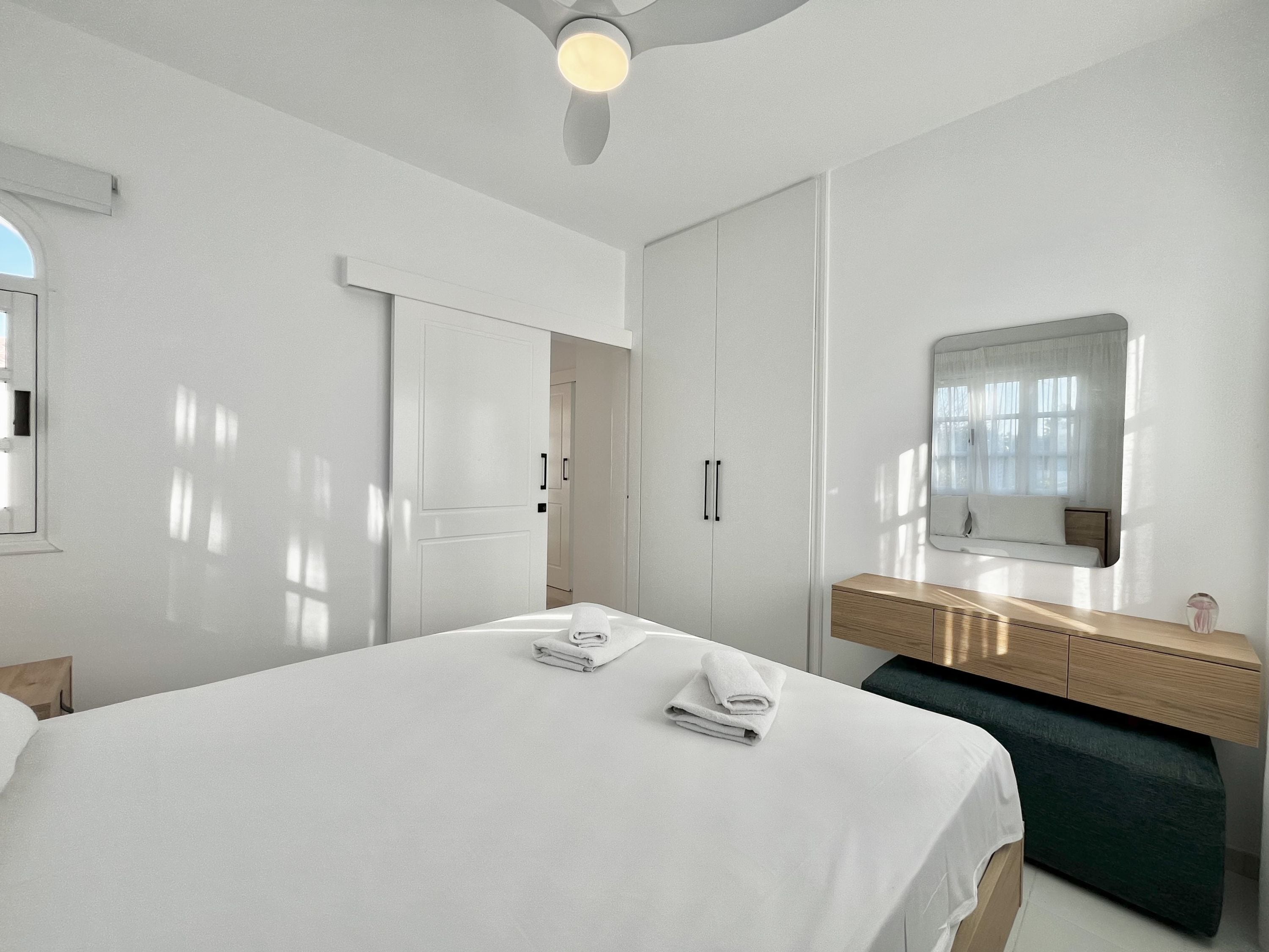 Una habitación de hotel moderna con una cama grande, un tocador de madera, un espejo y un ventilador de techo.