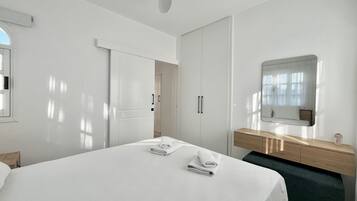 Una habitación de hotel moderna con una cama grande, un tocador de madera, un espejo y un ventilador de techo.