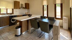A modern kitchen with a central island, built-in appliances, and a dining area with chairs. - 121 PEY - Stay Poseidon Villa (Pegeia)