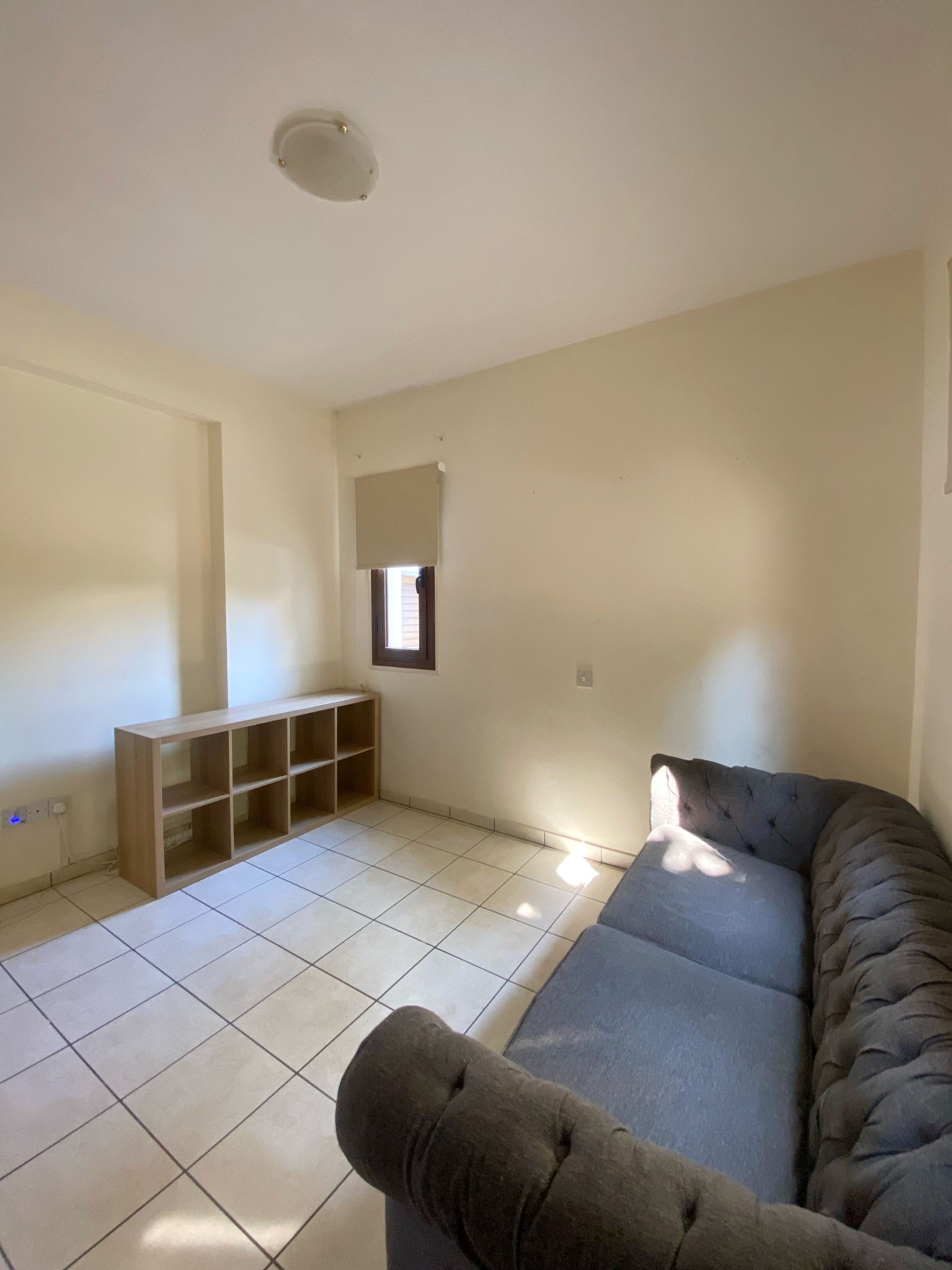 A living room with a sectional sofa, a wooden TV stand, and a window with blinds.
