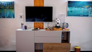 Een moderne woonkamer met een flatscreen televisie bevestigd aan een houten paneel, een koffiezetapparaat, een waterkoker en een klein kastje met een glazen vaas en een kaars.