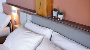 Een netjes opgemaakt bed met witte lakens en twee kleine planten in potten op het hoofdeinde.