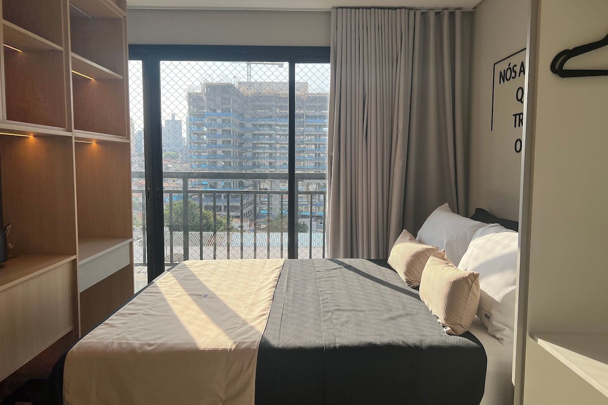 A hotel room with a bed, a wardrobe, a balcony with a view of buildings, and a sign on the wall.