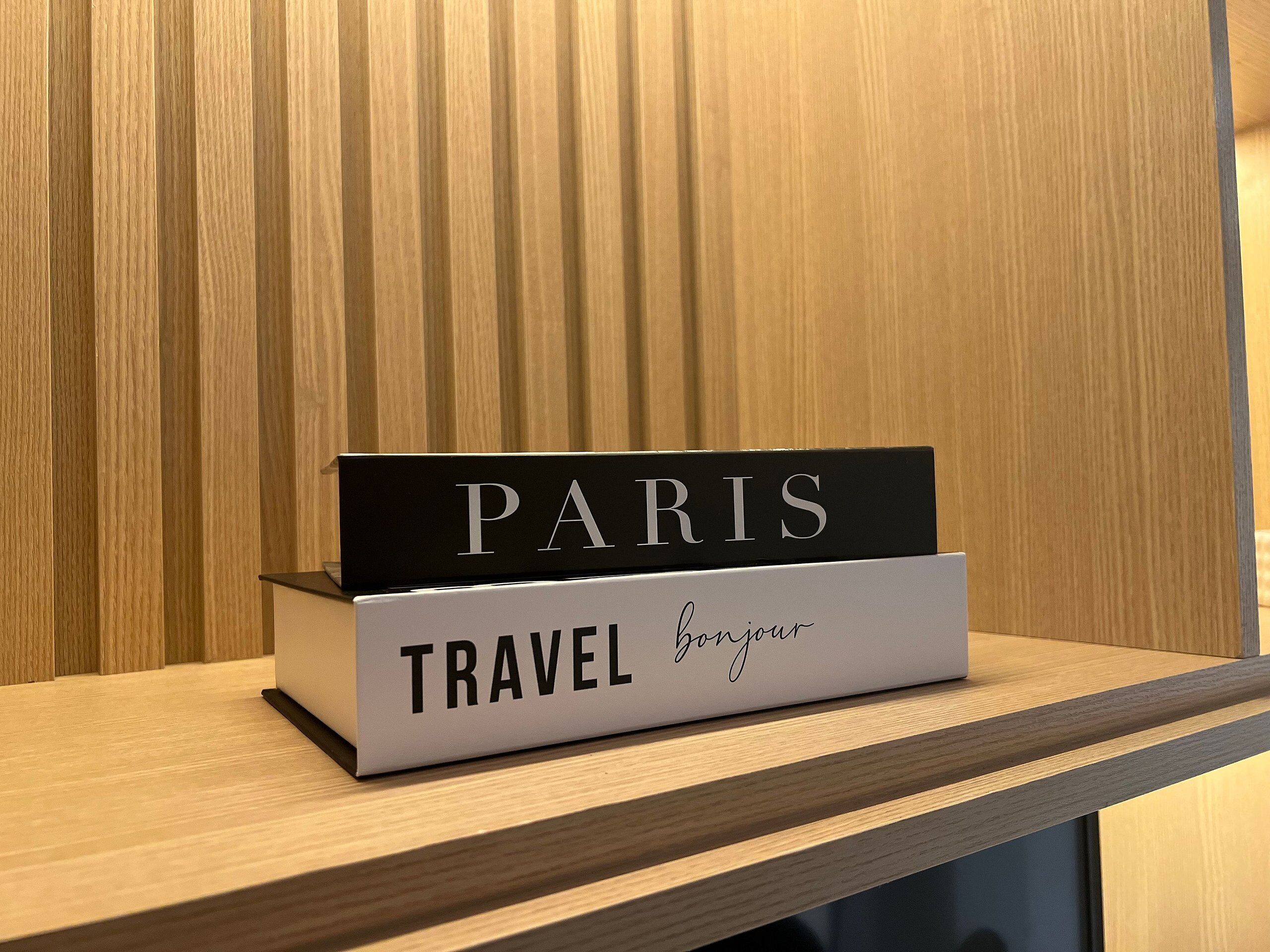 A wooden shelf with a black and white sign reading "PARIS" and "TRAVEL Bonjour".