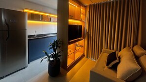 A modern living room with a sofa, a television, and a kitchen area with a refrigerator and microwave. - Infinity Home Suítes Anhembi (Sao Paulo)