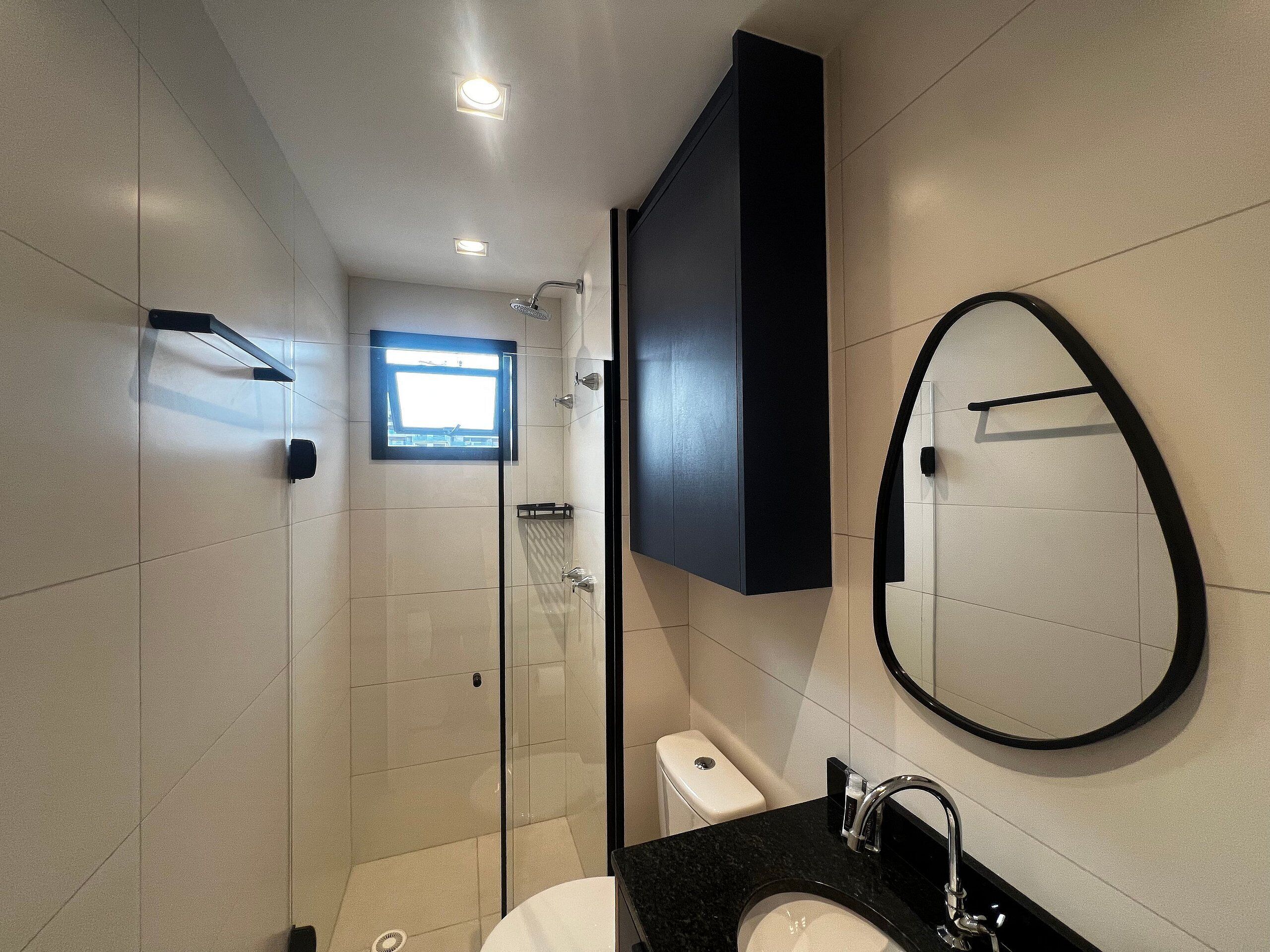 A modern bathroom with a glass-enclosed shower, a black sink, and a large oval mirror.