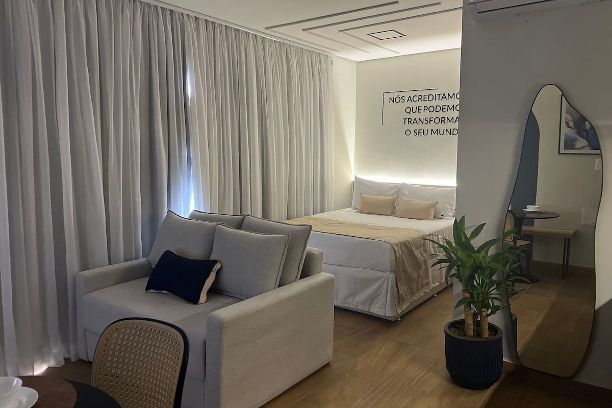 A modern hotel room with a bed, a sofa, a small table, and a potted plant.