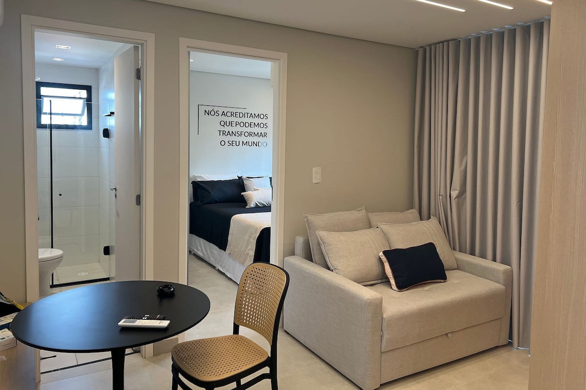 A modern hotel room with a sofa, a chair, a small table, and a bed with a window.