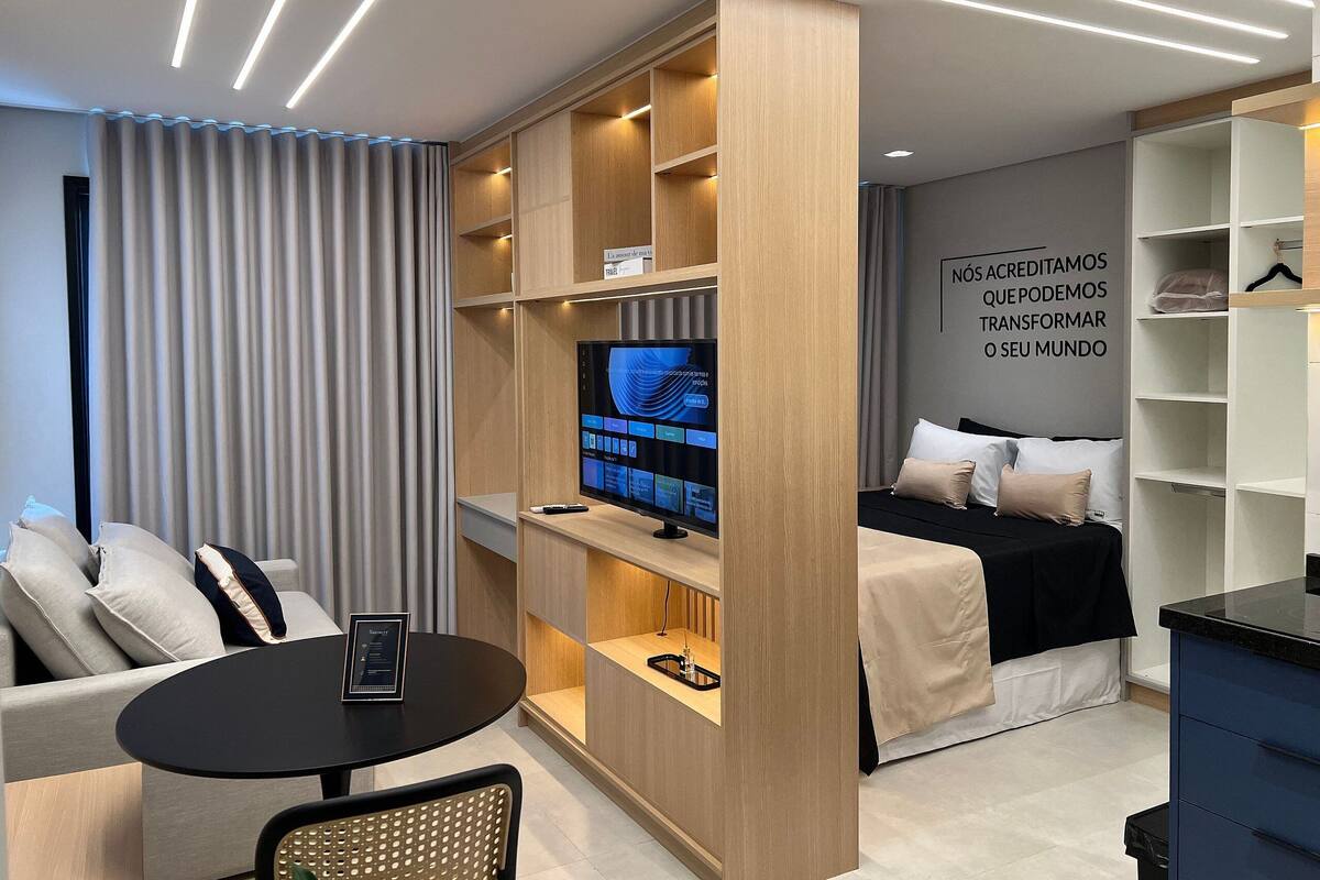 A modern hotel room with a TV, a sofa, a dining table, and a wardrobe.