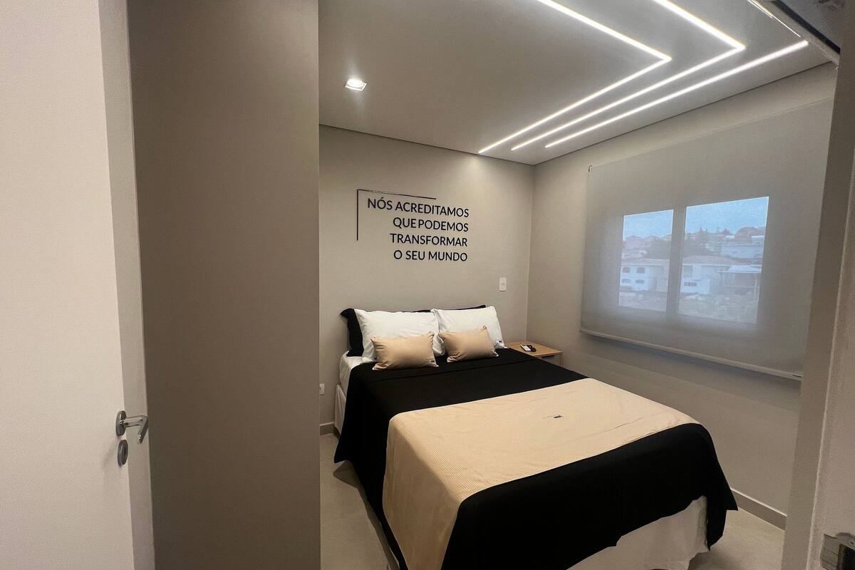 A modern bedroom with a bed, a projector screen, and a motivational quote on the wall.
