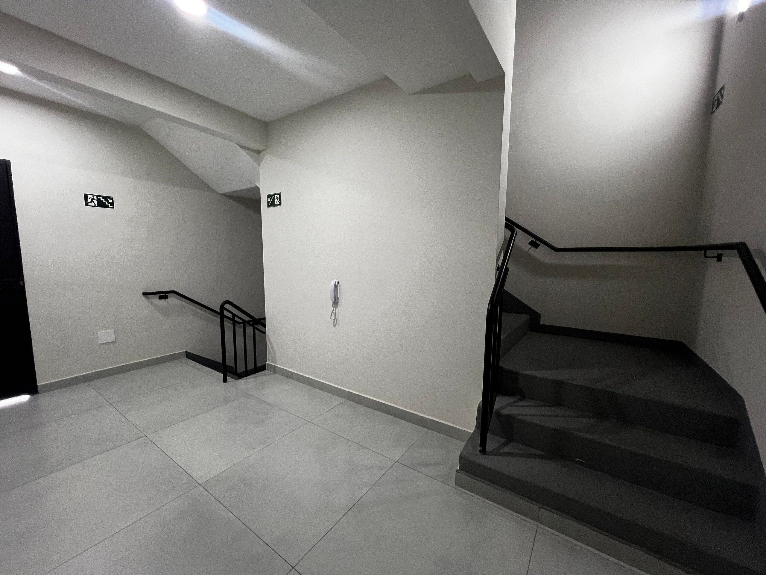 Una escalera moderna y limpia con barandilla, un portero automático en la pared y una puerta al final.