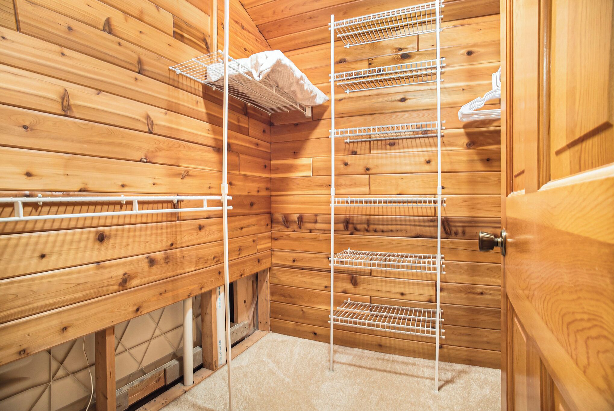 Interior de una cabaña de madera con un estante empotrado y una puerta.
