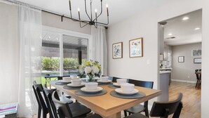 Een eetgedeelte met een houten tafel voor zes personen, zwarte stoelen, een kroonluchter en uitzicht door een raam.