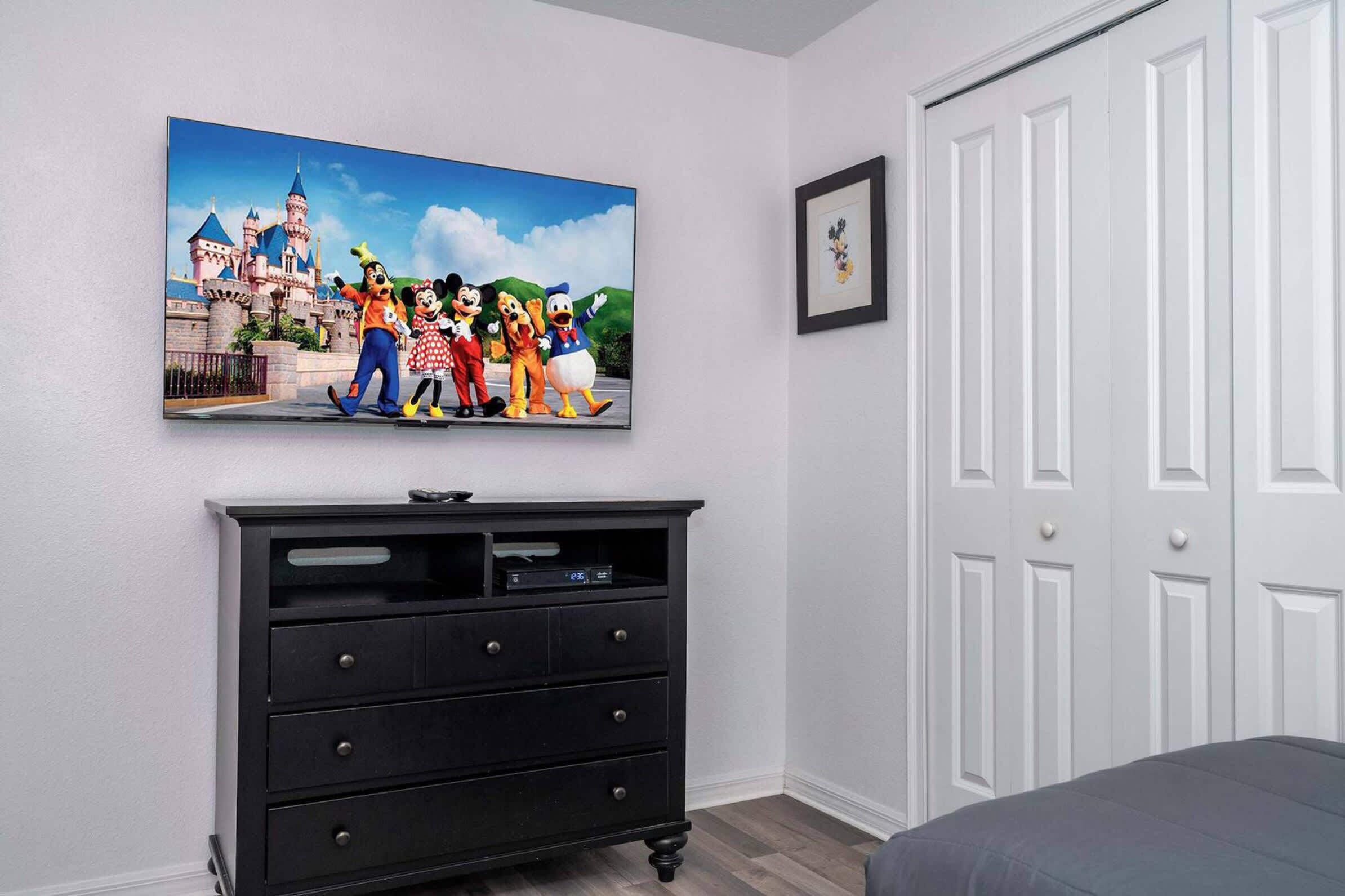 A bedroom with a large Disney-themed painting, a black dresser, a framed picture, and white doors.