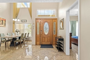 Un'ampia zona giorno con tavolo e sedie, una porta in legno con vetri decorativi e vista sull'esterno attraverso una finestra.