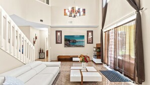 A spacious living room with a white sofa, a coffee table, and a painting on the wall. - Jasmine Breeze Home for 12 (Kissimmee)