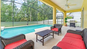 A covered outdoor area with a pool, wicker furniture, and a barbecue grill. - Jasmine Breeze Home for 12 (Kissimmee)