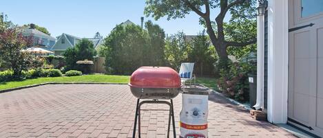 A barbecue grill and a bag of charcoal in a driveway.