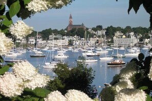 A marina with numerous boats docked, a prominent clock tower in the background, and a backdrop of residential buildings. - Refined Comfort in the Heart of Marblehead (Marblehead)