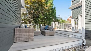 Een overdekt terras buiten met rieten meubels en een witte balustrade.