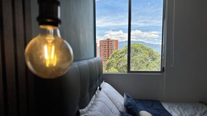 Une chambre à coucher avec un lit, des oreillers et une vue sur le paysage urbain, visible par la fenêtre.