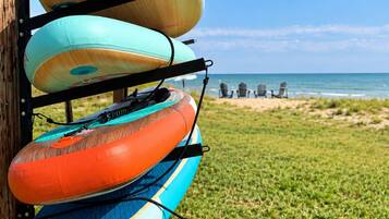 A rack of kayaks against a wooden post with a beach and ocean in the background.
