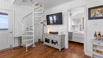 Une pièce avec un escalier en colimaçon, un téléviseur à écran plat, un lit, un petit meuble contenant des bouteilles de vin et un tableau encadré accroché au mur.