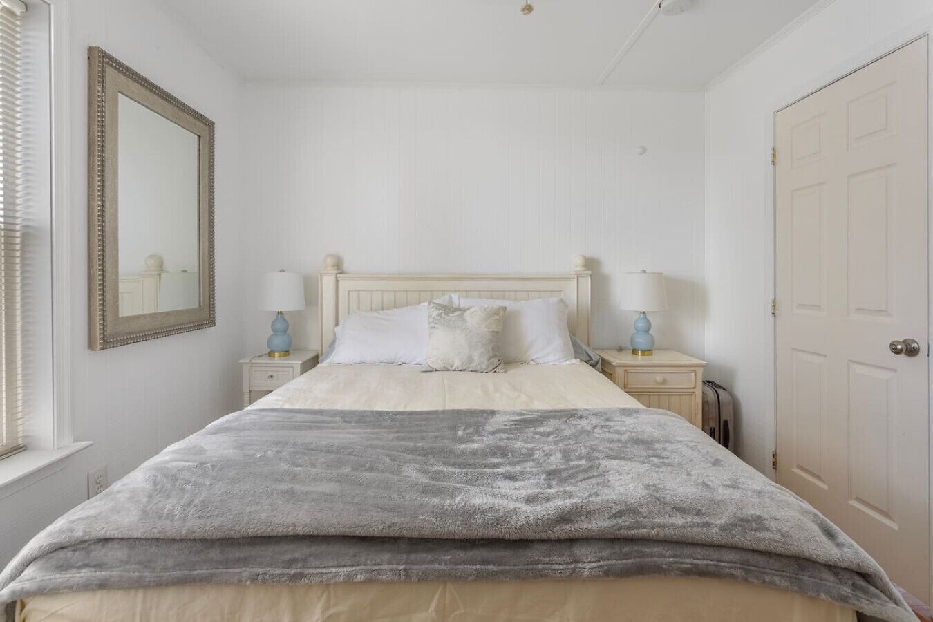 A bedroom with a bed, two bedside tables, a nightstand, a mirror, and a door.
