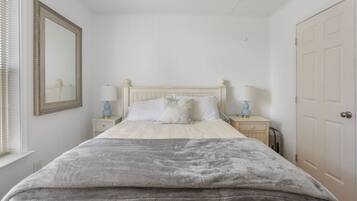 A bedroom with a bed, two bedside tables, a nightstand, a mirror, and a door.