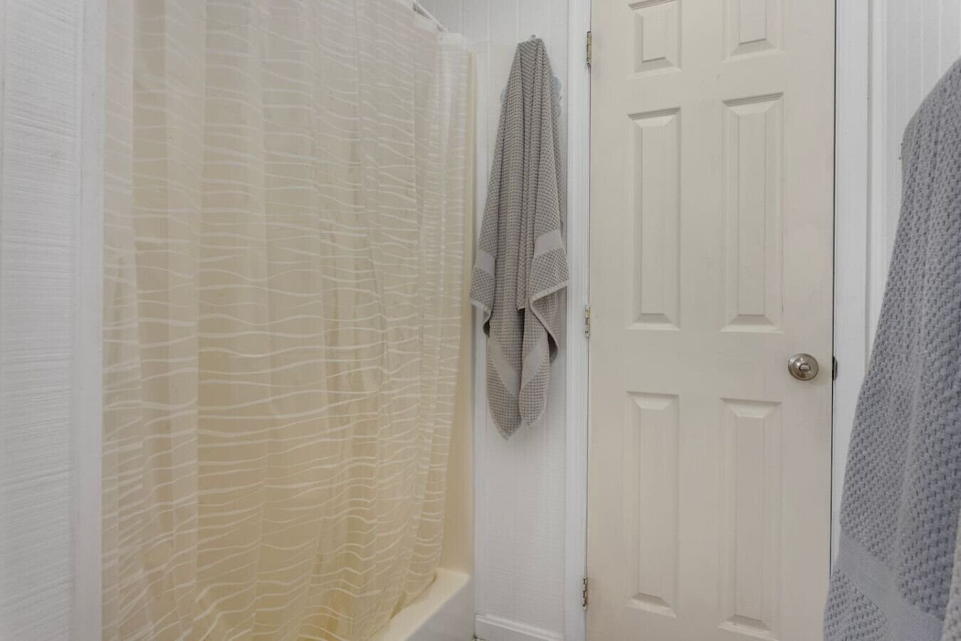 Un baño con cortina de ducha, una toalla colgada en la pared y una puerta blanca.