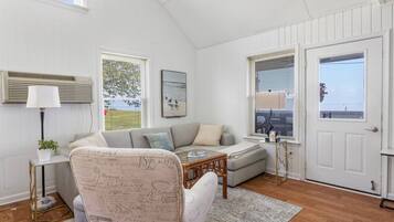 A cozy living room with a sofa, armchair, and coffee table, a side table with a lamp, and a door with a window.