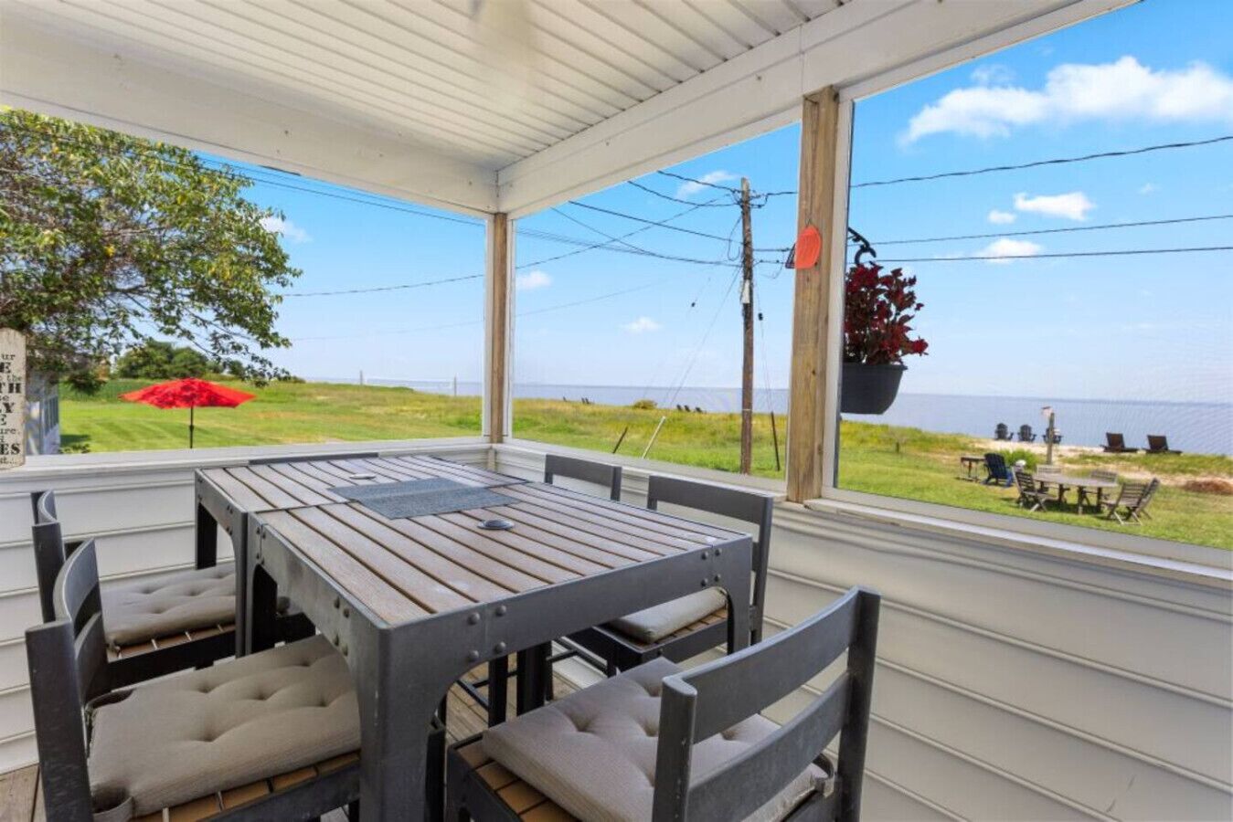 A covered patio with a table and chairs, a hanging planter, and a view of the sea.