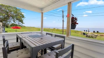 A covered patio with a table and chairs, a hanging planter, and a view of the sea.