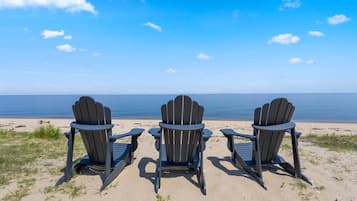 Three Adirondack chairs facing a beach with a clear view of the ocean.