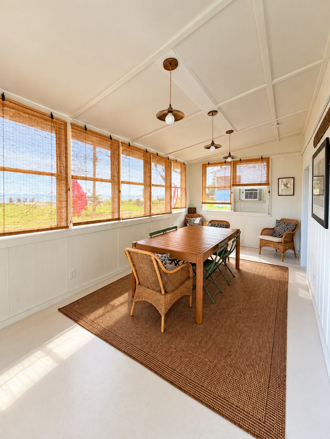 A dining area with a wooden table and chairs, large windows with bamboo blinds, and a ceiling with exposed beams and pendant lights.