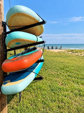 A rack of kayaks against a wooden post with a beach and ocean in the background.