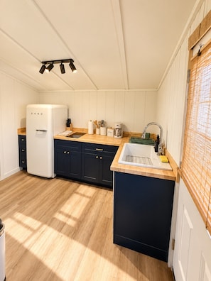 A compact kitchen with a white refrigerator, dark cabinets, a wooden countertop, and a sink with a faucet.