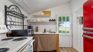 A compact kitchen with a stove, sink, and a red refrigerator.