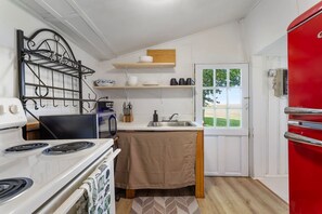 A compact kitchen with a stove, sink, and a red refrigerator.