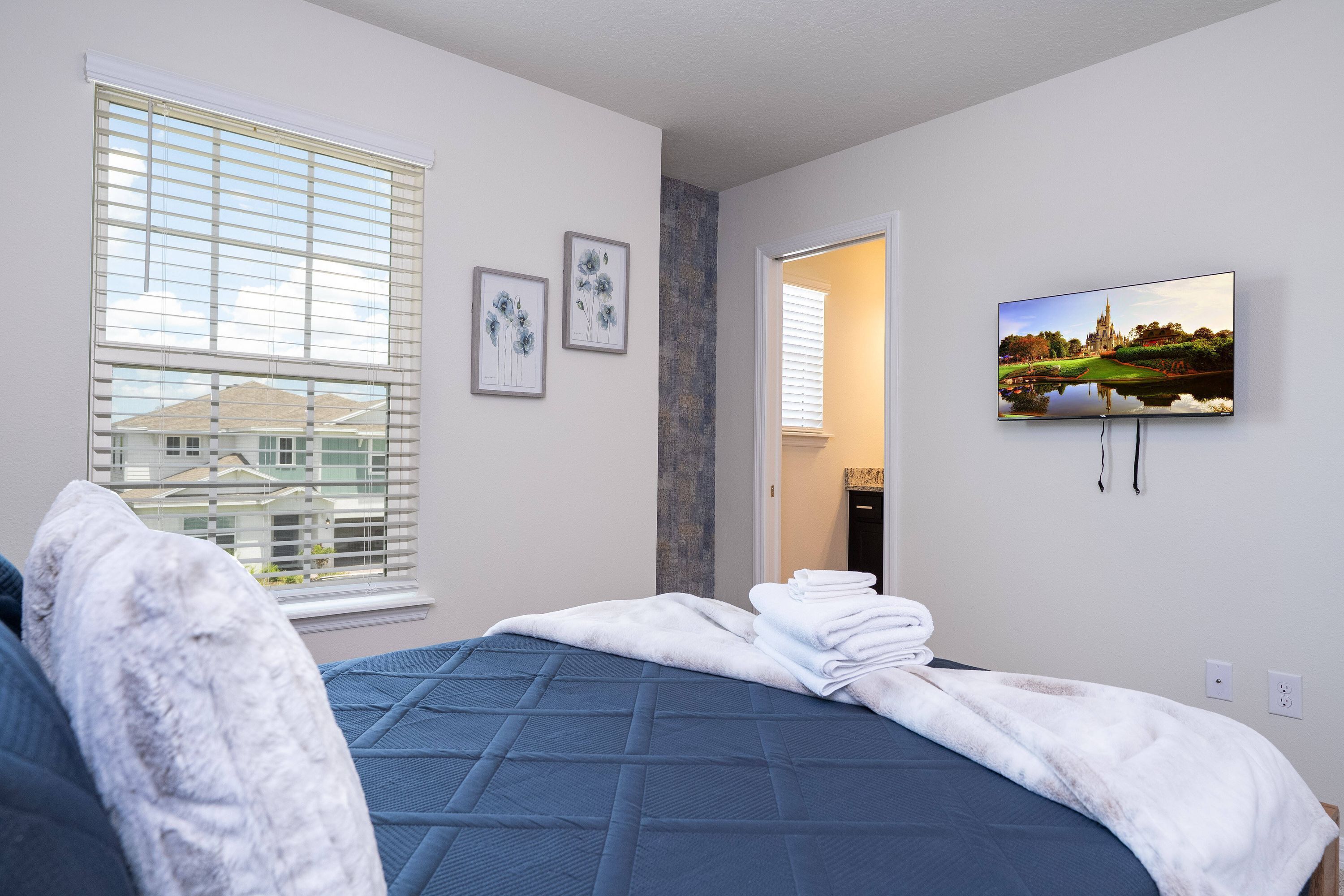 Ett sovrum med en säng, en tv på väggen och ett fönster med persienner.