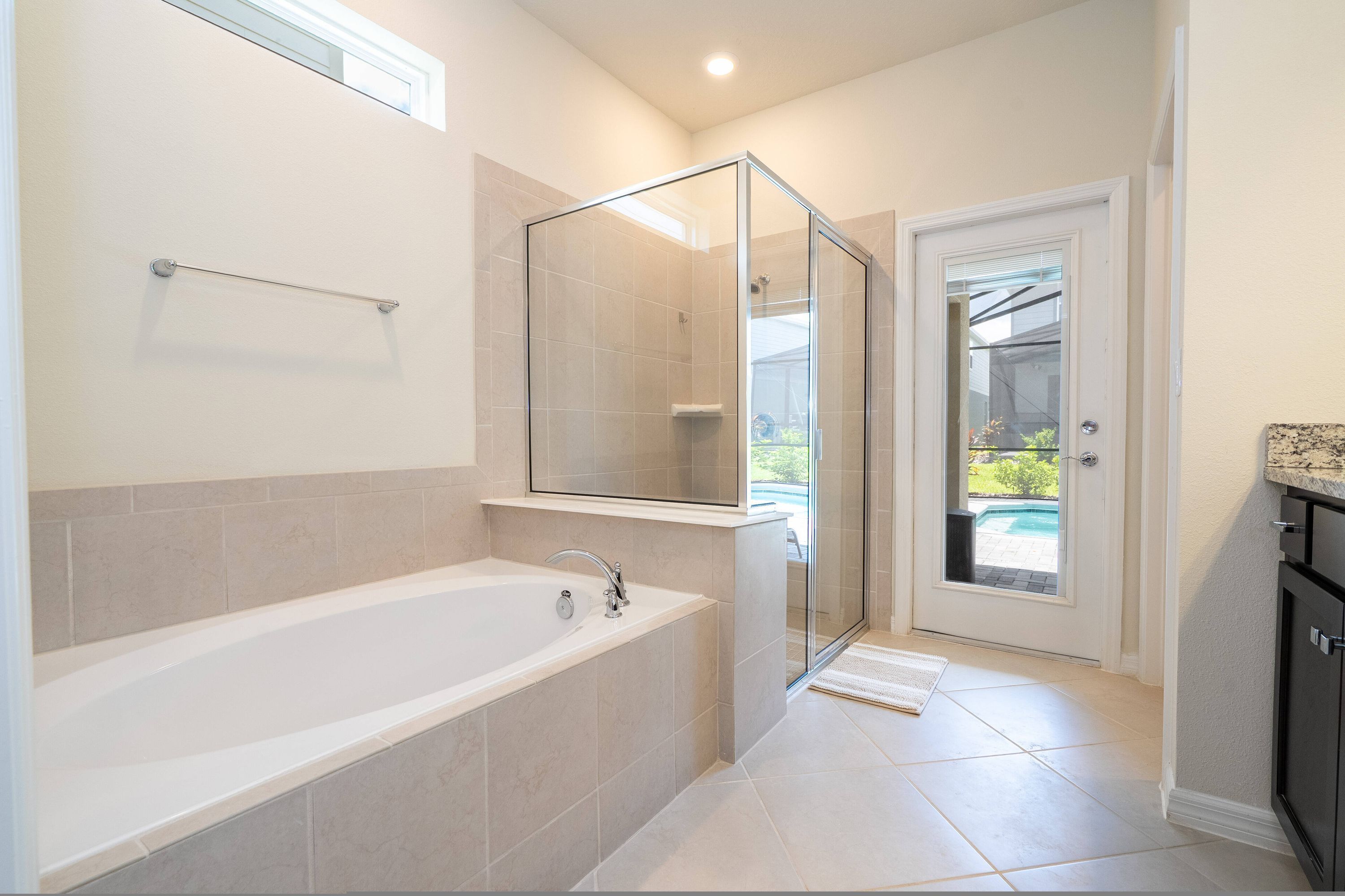 Un baño moderno con ducha envuelta en vidrio, una bañera grande y vista a una piscina a través de una puerta.