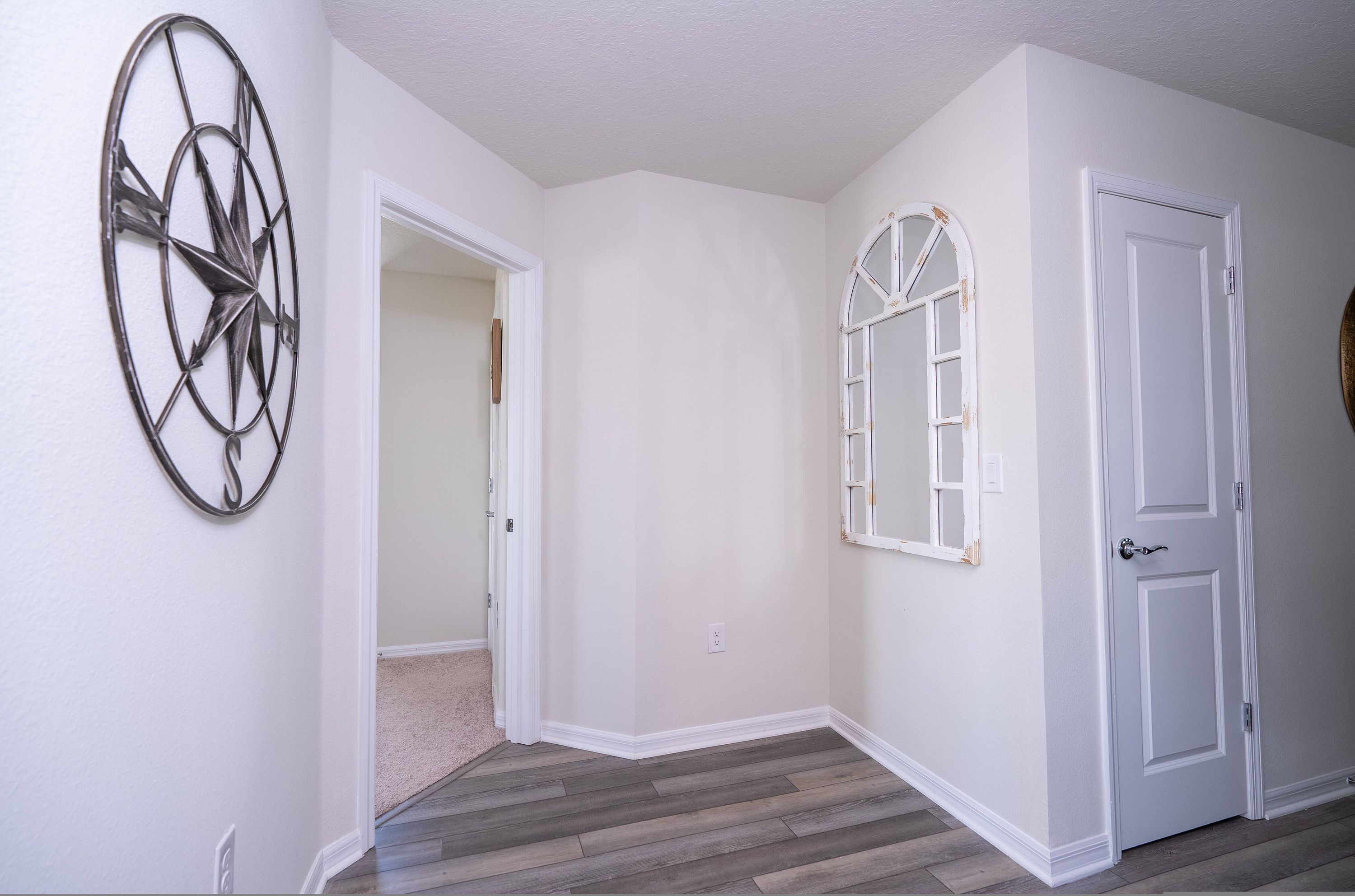 Un couloir aux murs blancs, doté d’un plancher en bois, d’un élément décoratif en métal et d’une porte blanche.