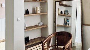 Una stanza con una sedia di legno, una libreria piena di oggetti e uno specchio che riflette l'ambiente.