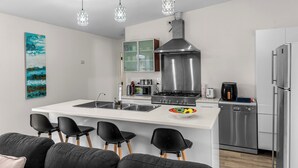 A modern kitchen with a central island, stainless steel appliances, and pendant lighting. - Anchors Away - Mangawhai Heads Holiday Home (Mangawhai)