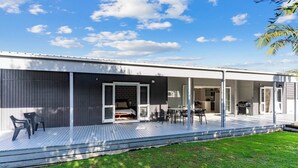 A modern house with a covered patio, a dining area, and a barbecue. - Anchors Away - Mangawhai Heads Holiday Home (Mangawhai)
