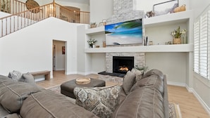 A spacious living room with a fireplace, a large flat-screen TV, and a staircase leading to an upper level. - Splash Canyon - Splash Pad & Tons of Games - Gym (Chandler)