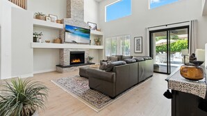 A spacious living room with a fireplace, a large sofa, and a view of the outdoors through a sliding glass door. - Splash Canyon - Splash Pad & Tons of Games - Gym (Chandler)